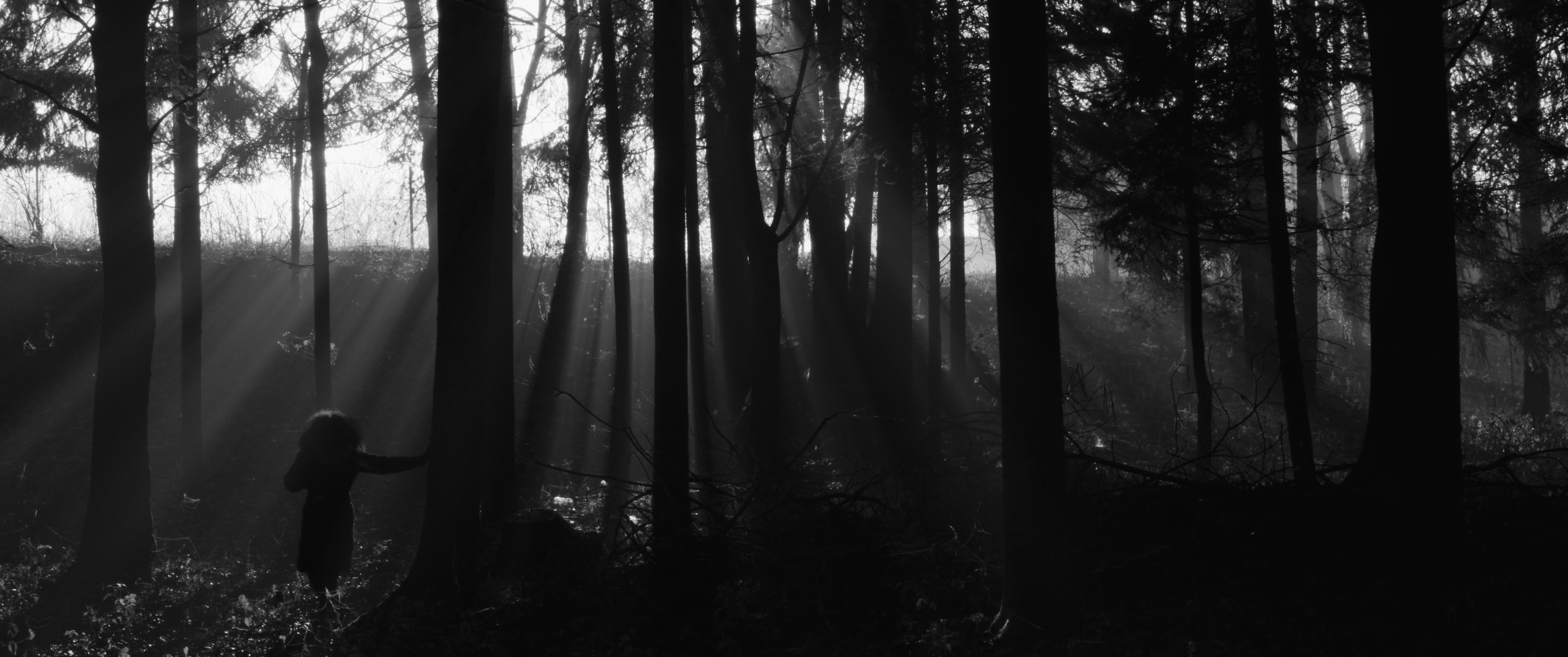 Black and white photograph of Gheorghe and Sorina, his wife. Gheroghe is sitting at a table in the courtyard of their house, talking and looking at her. Sorina is standing with her hand on the back of the chair, looking at him.