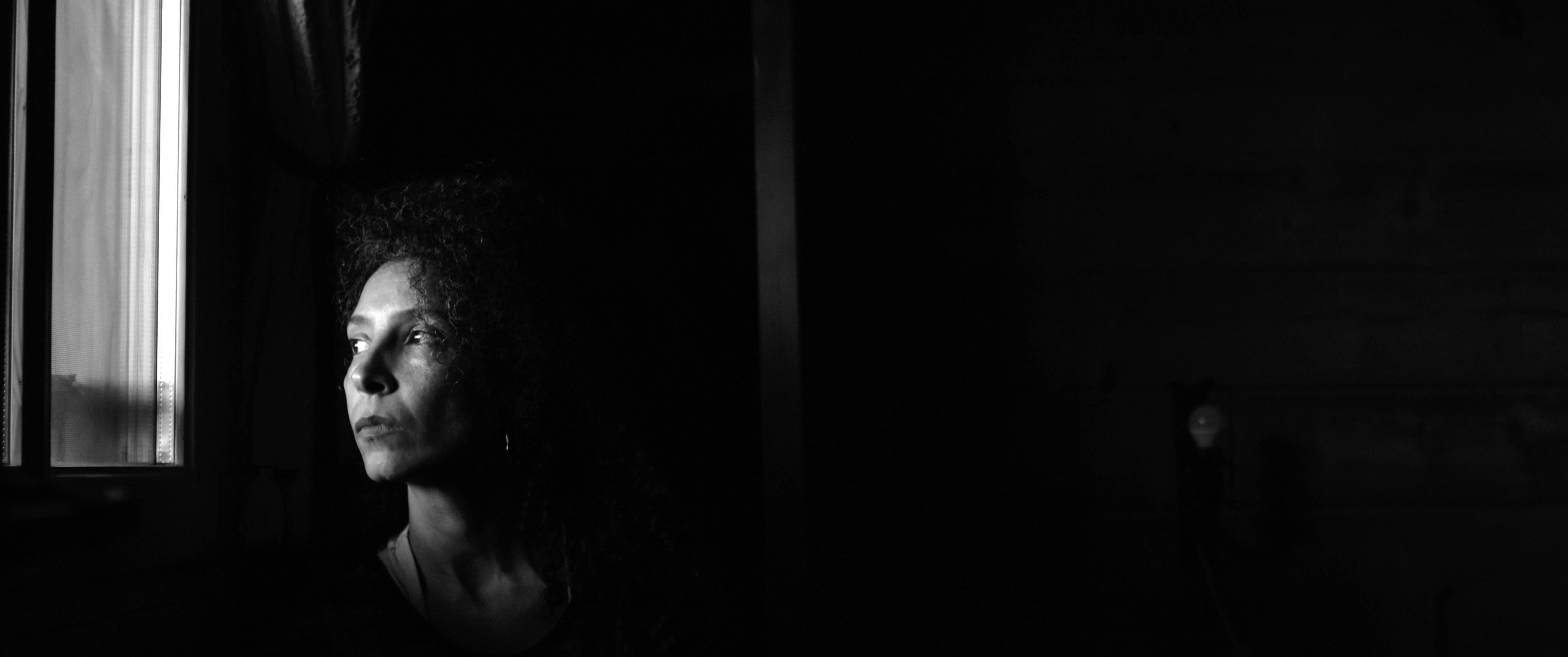 Black and white photograph of Gheorghe sitting on a bench. He is staring into the camera and holding out a photograph of himself playing the violin when he was younger. 